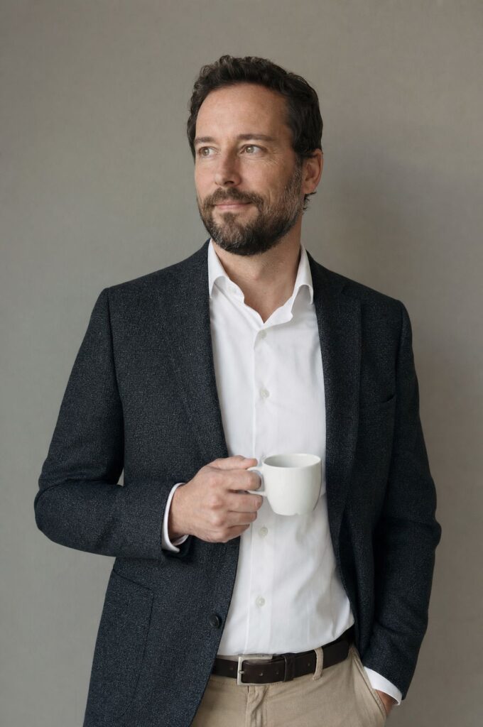 Ein Anwalt steht mit einer Kaffeetasse vor einer ruhigen grauen Wand.